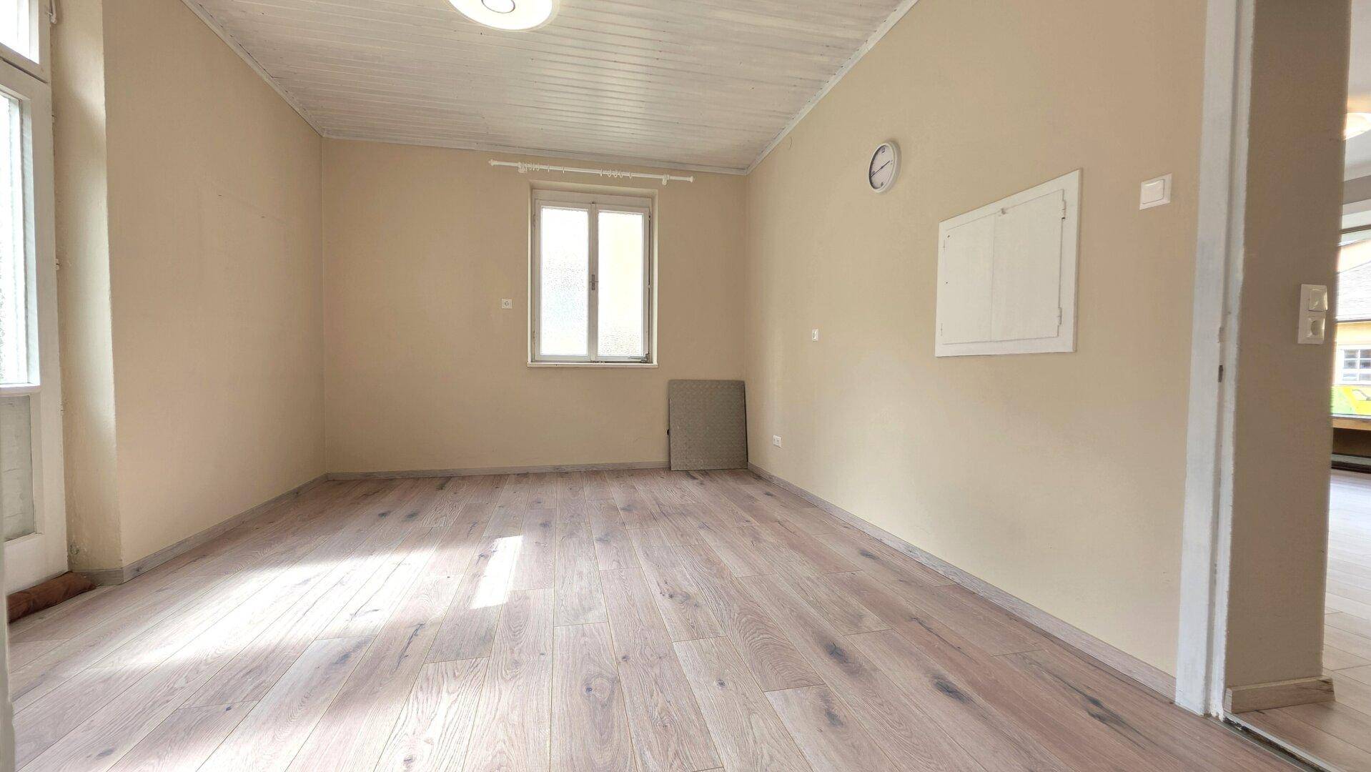 Leerer Raum mit hellem Holzboden und einem Fenster, das für natürliche Belichtung sorgt.