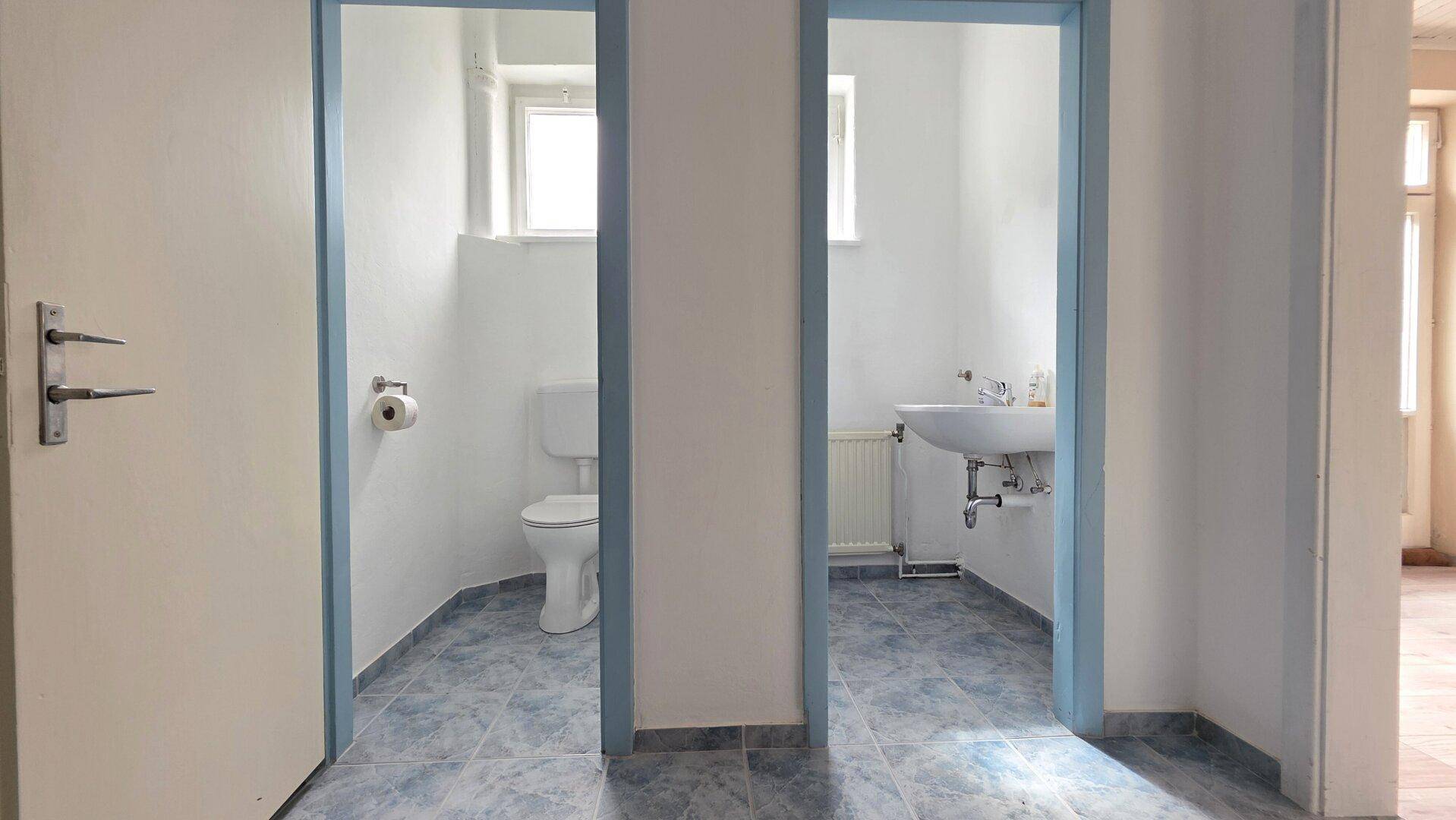Zwei separate Toilettenbereiche mit Waschbecken und Fenstern, funktional gestaltet.
