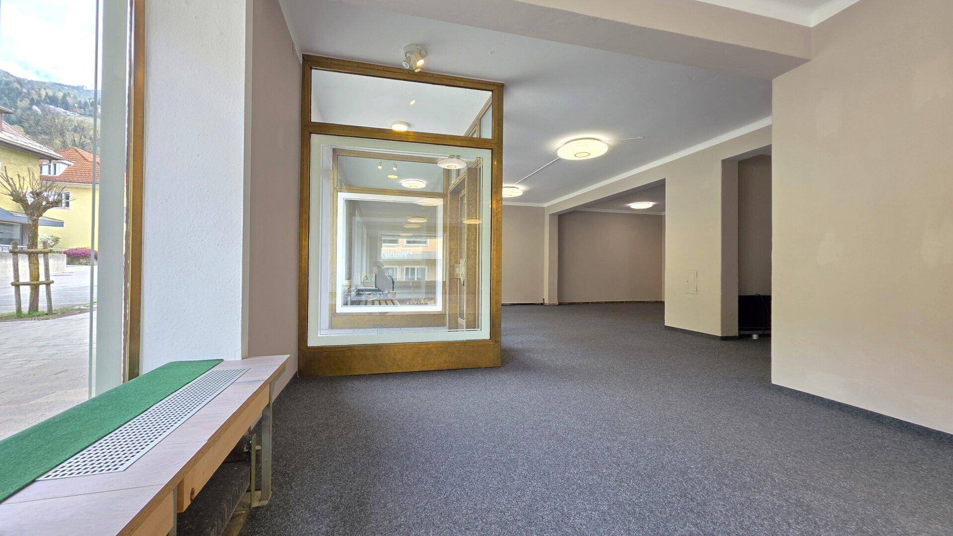 Großer, leerer Raum mit Teppichboden und einer gläsernen Vitrine oder Eingangsbereich.