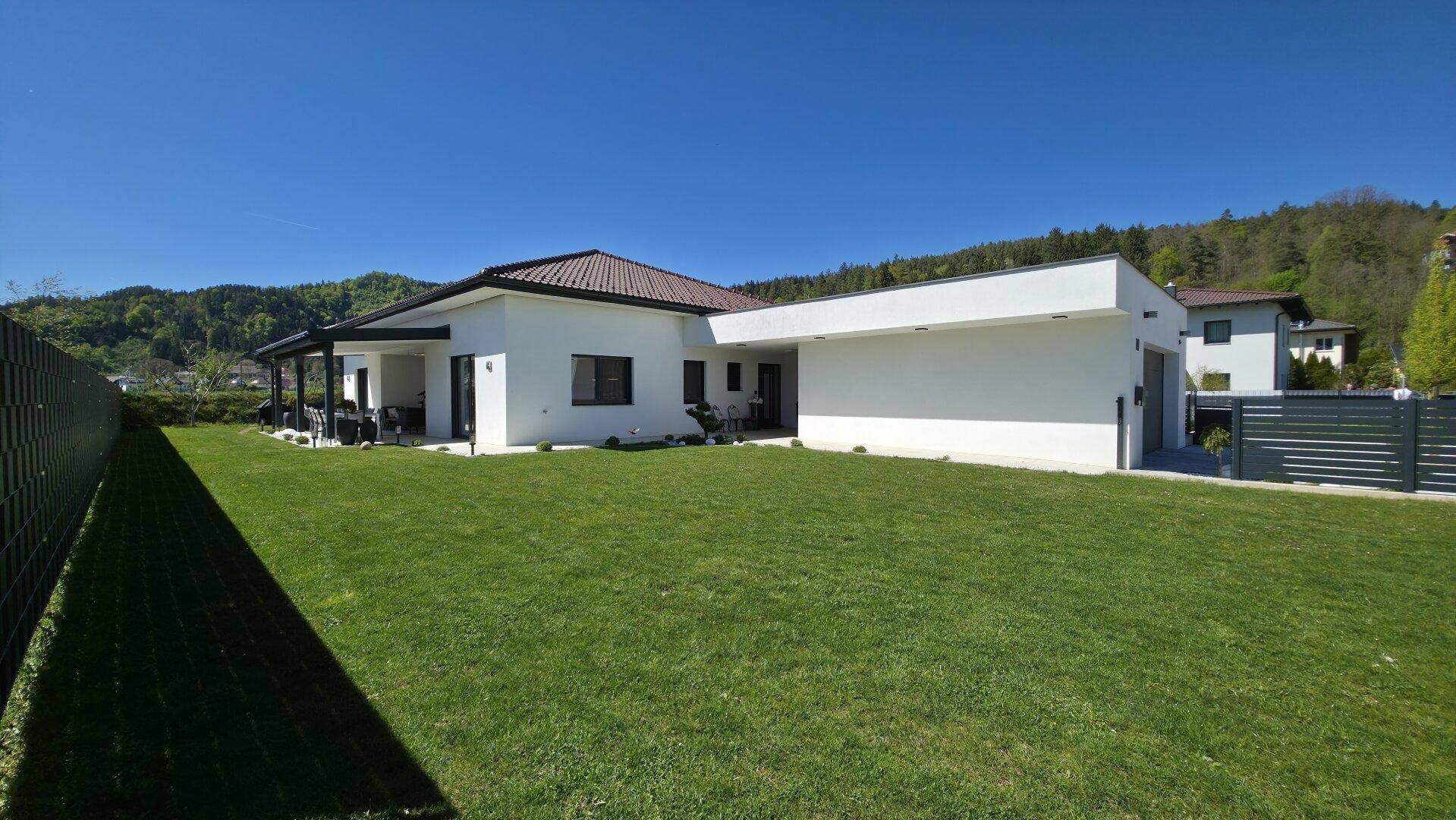 Seitenansicht des modernen Hauses mit weitläufiger Rasenfläche und Blick auf die umliegende Natur.