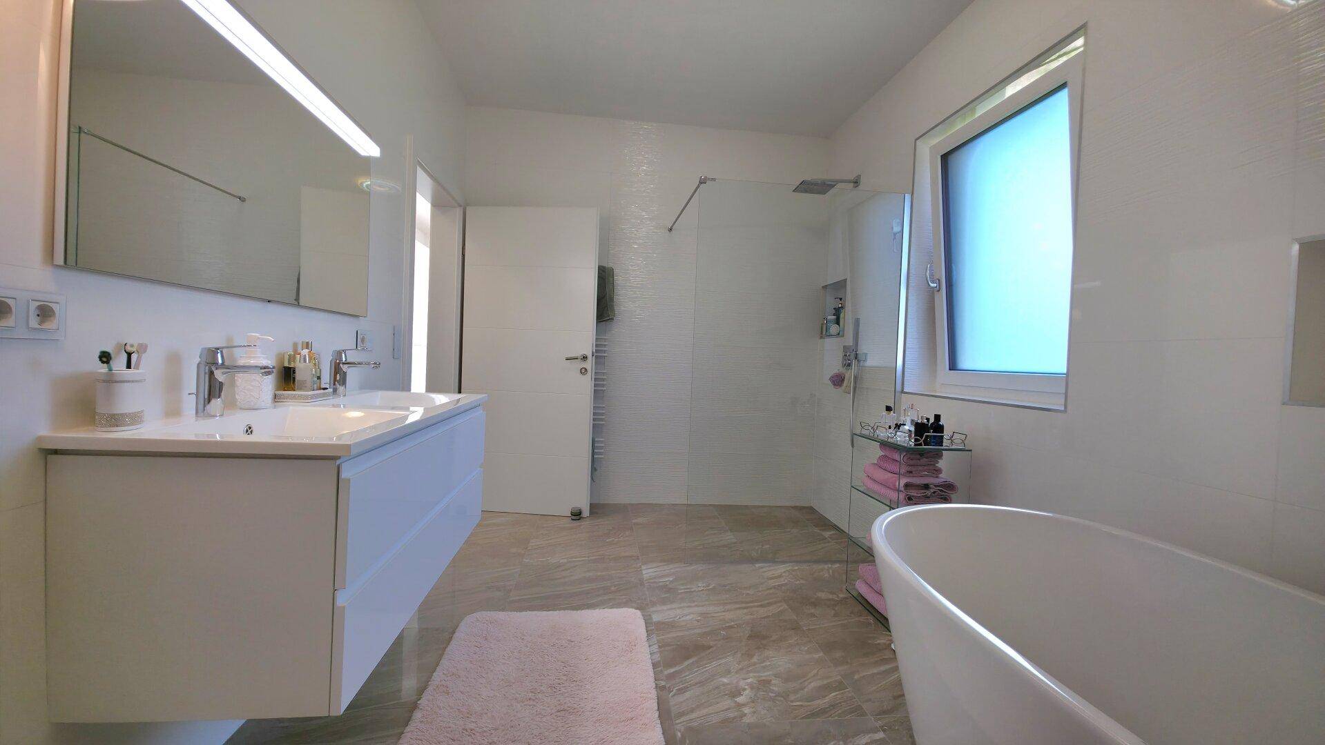 Modernes Badezimmer mit freistehender Badewanne, großer Dusche und Doppelwaschbecken, hell und geräumig.