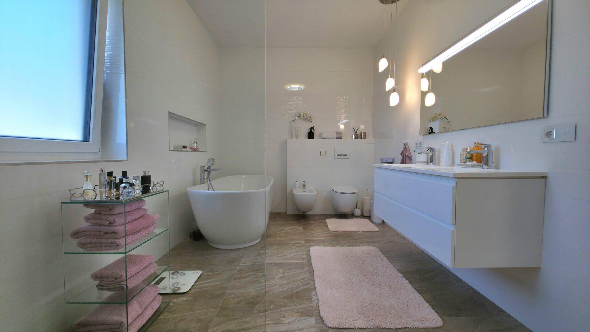 Elegantes Badezimmer mit freistehender Badewanne, Bidet und modernem Doppelwaschbecken, in hellen Farbtönen.