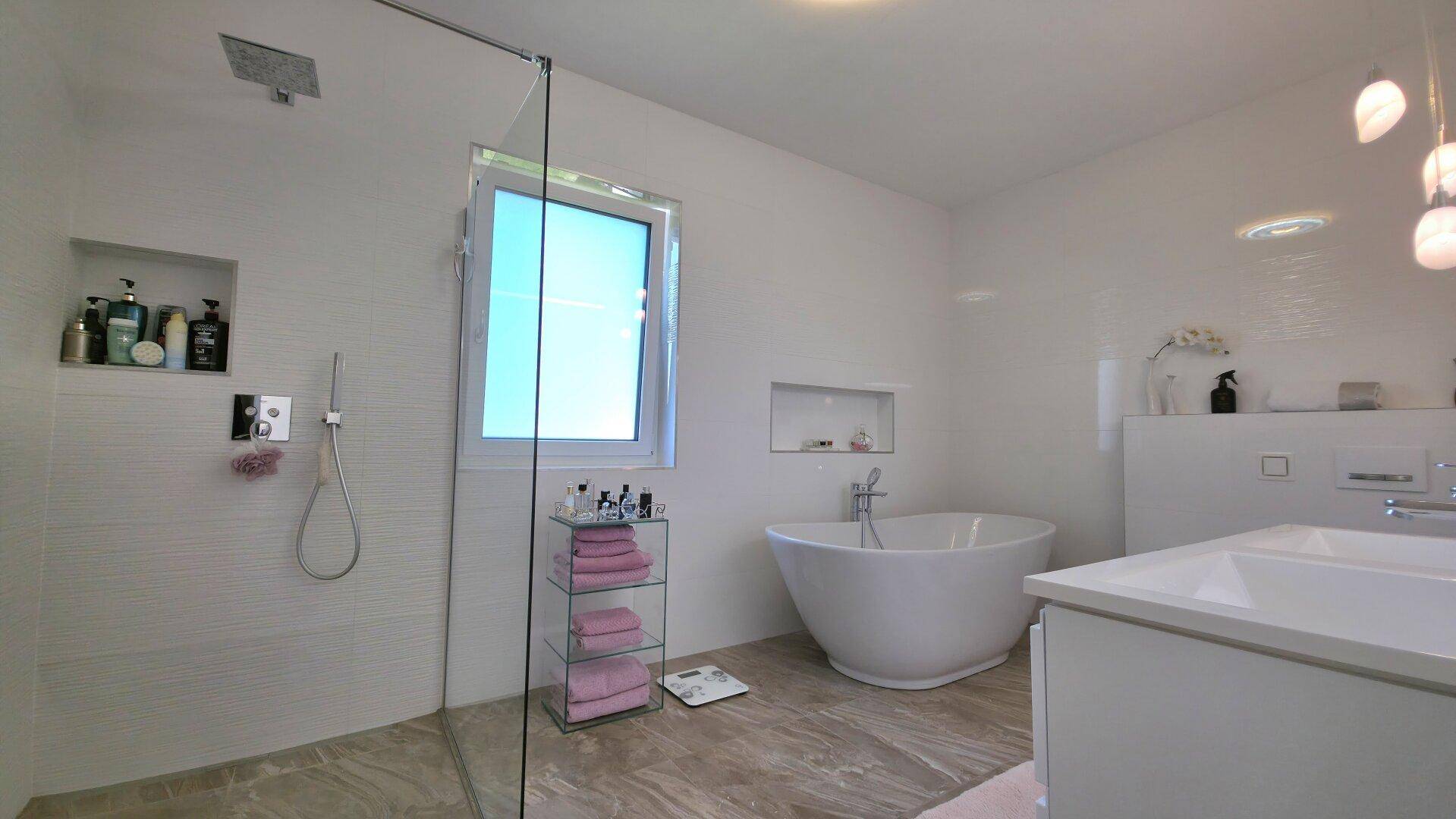 Geräumiges Badezimmer mit großer begehbarer Dusche, freistehender Badewanne und Fenster für Tageslicht.