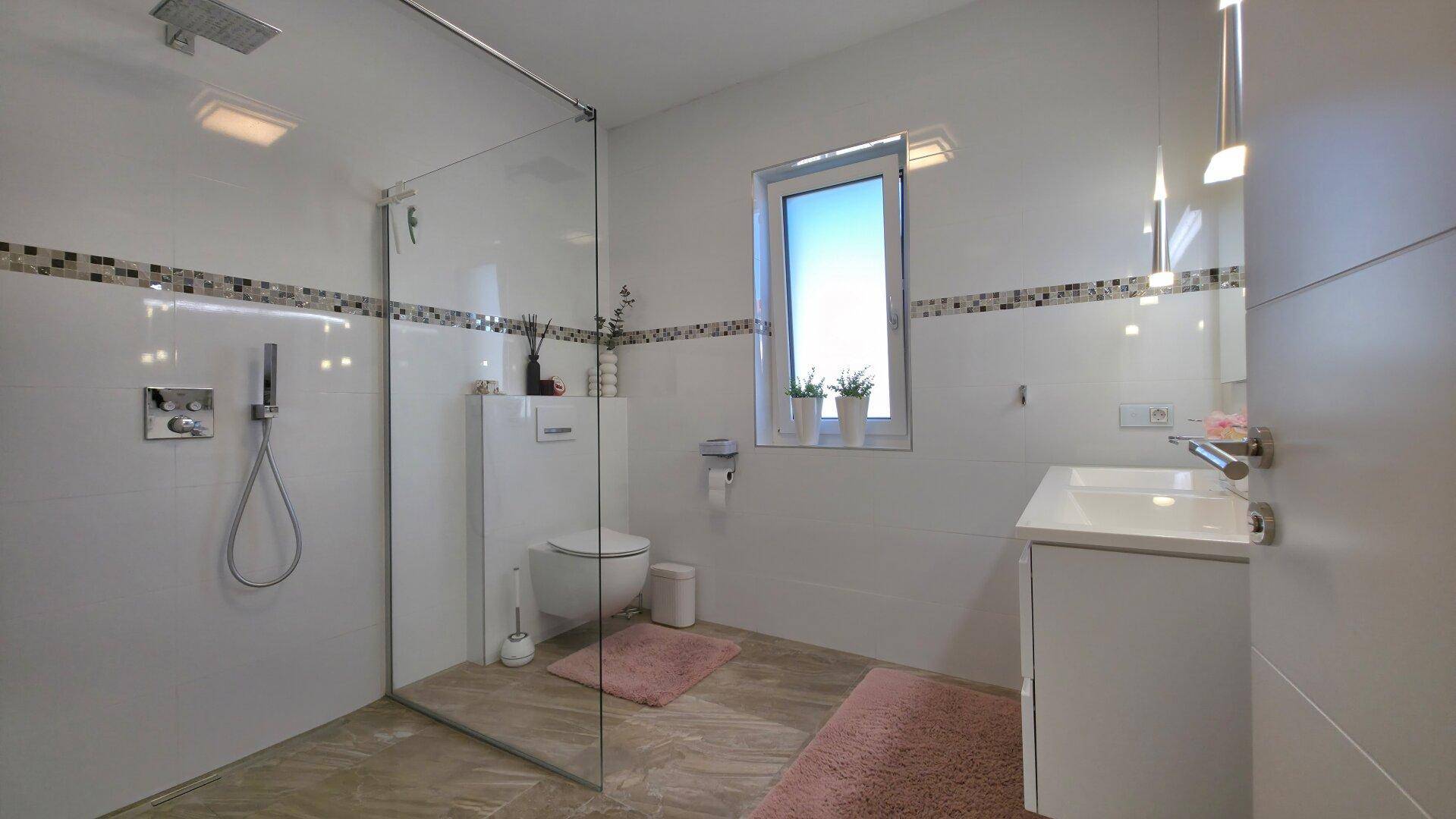 Modernes Badezimmer mit begehbarer Dusche, wandhängendem WC und Fenster, ausgestattet mit stilvollen Fliesen.