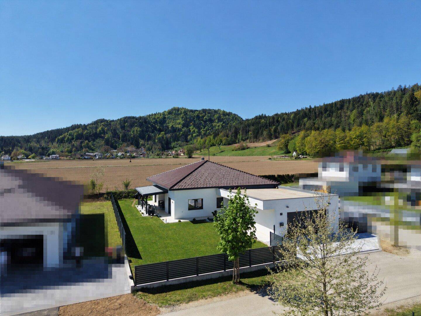 Luftaufnahme eines modernen Einfamilienhauses mit Garten und Blick auf die umliegende Landschaft und Hügel.
