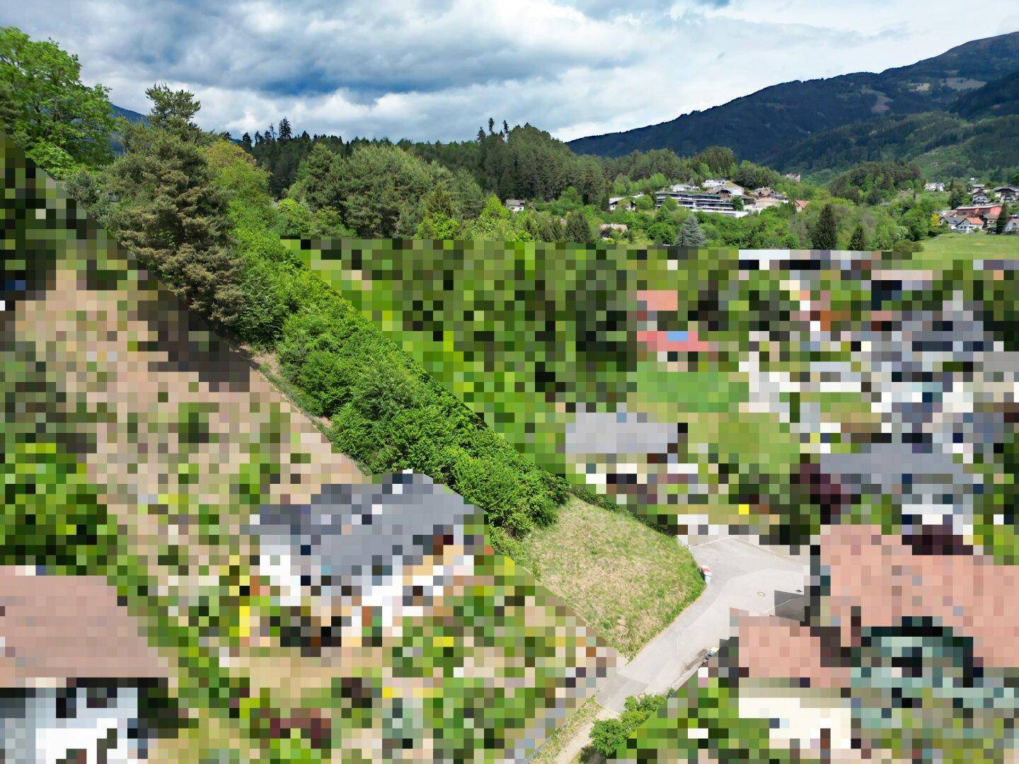Panoramablick auf eine hügelige Landschaft mit Häusern, Wäldern und Bergen unter bewölktem Himmel.