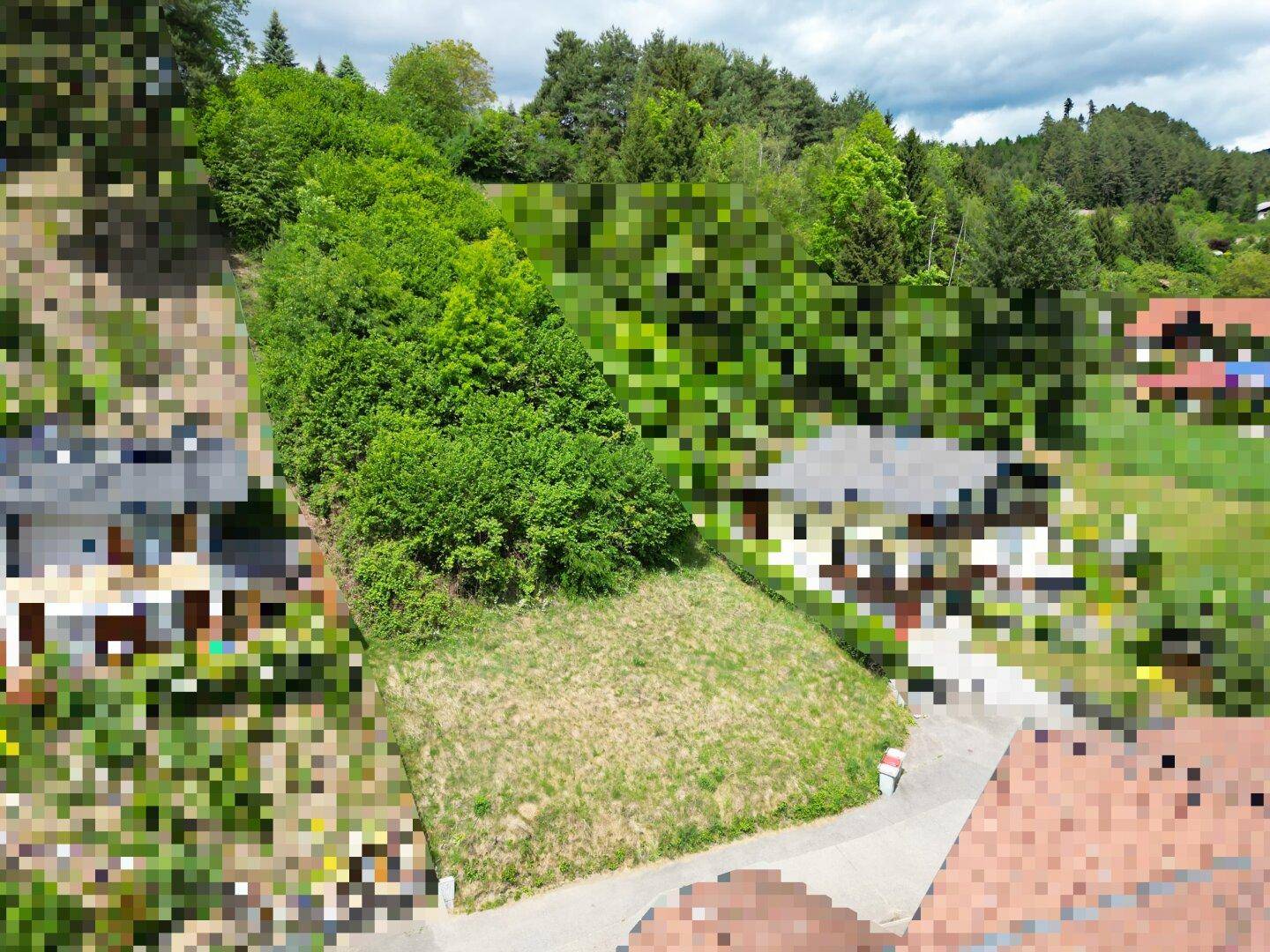 Luftaufnahme eines unbebauten Grundstücks an einem Hang, umgeben von Bäumen und Wohnhäusern.