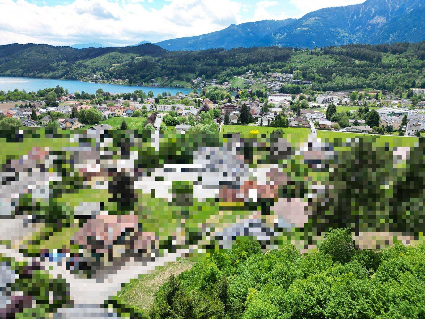Weitläufige Luftaufnahme eines Dorfes am See mit umliegenden grünen Hügeln und Bergen.