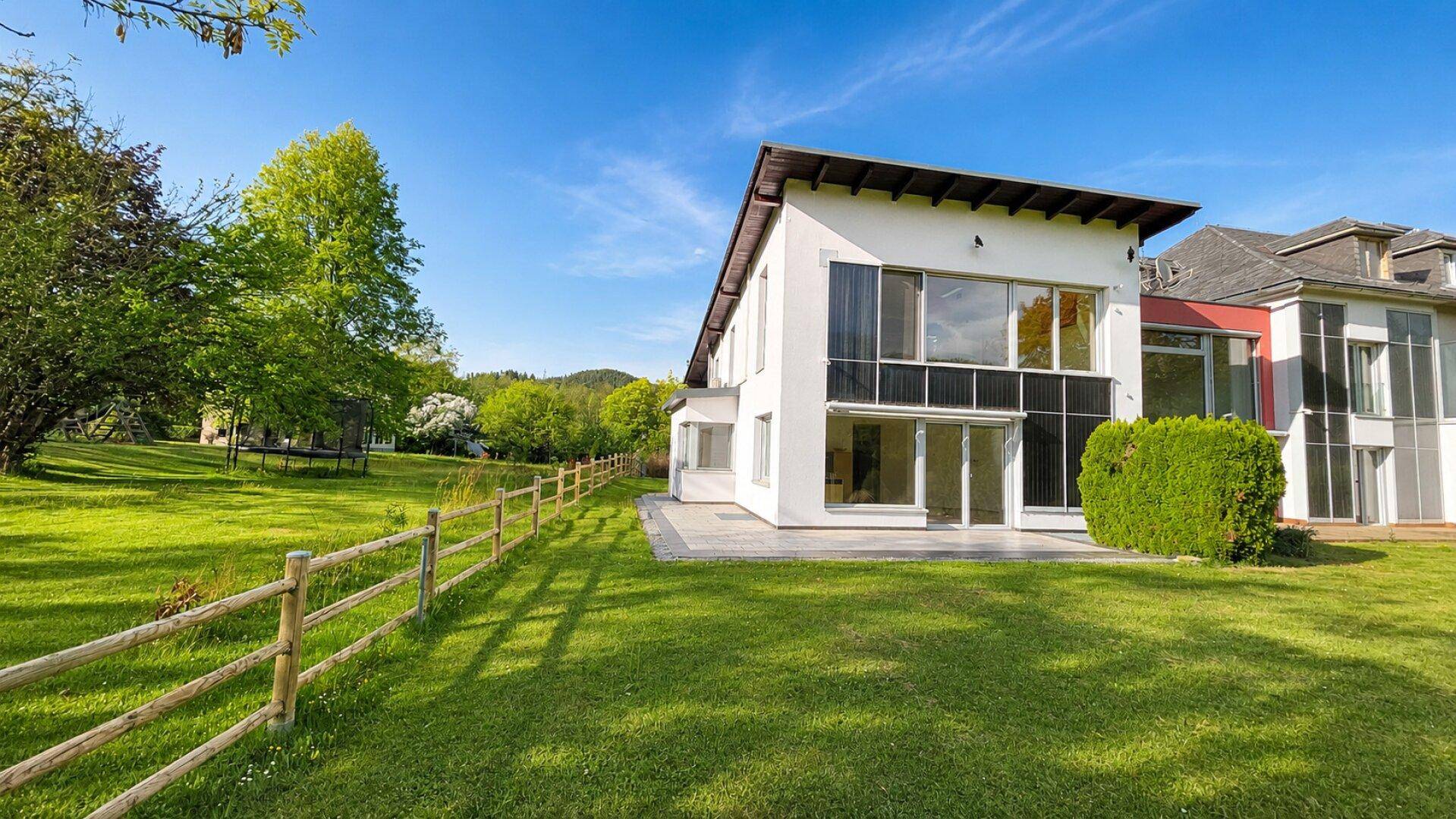 Moderne Hausfassade mit weitläufigem Rasen und Holzzaun in einer grünen Umgebung.