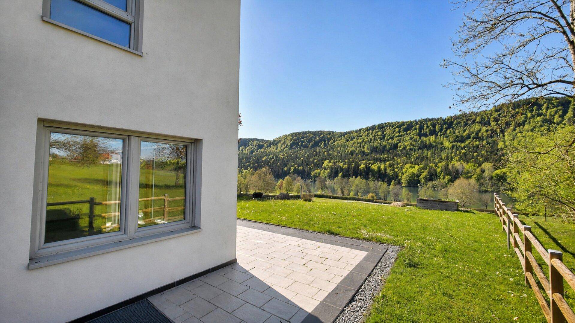 Gepflasterte Terrasse am Haus mit weitem Blick auf den See und die bewaldeten Hügel.