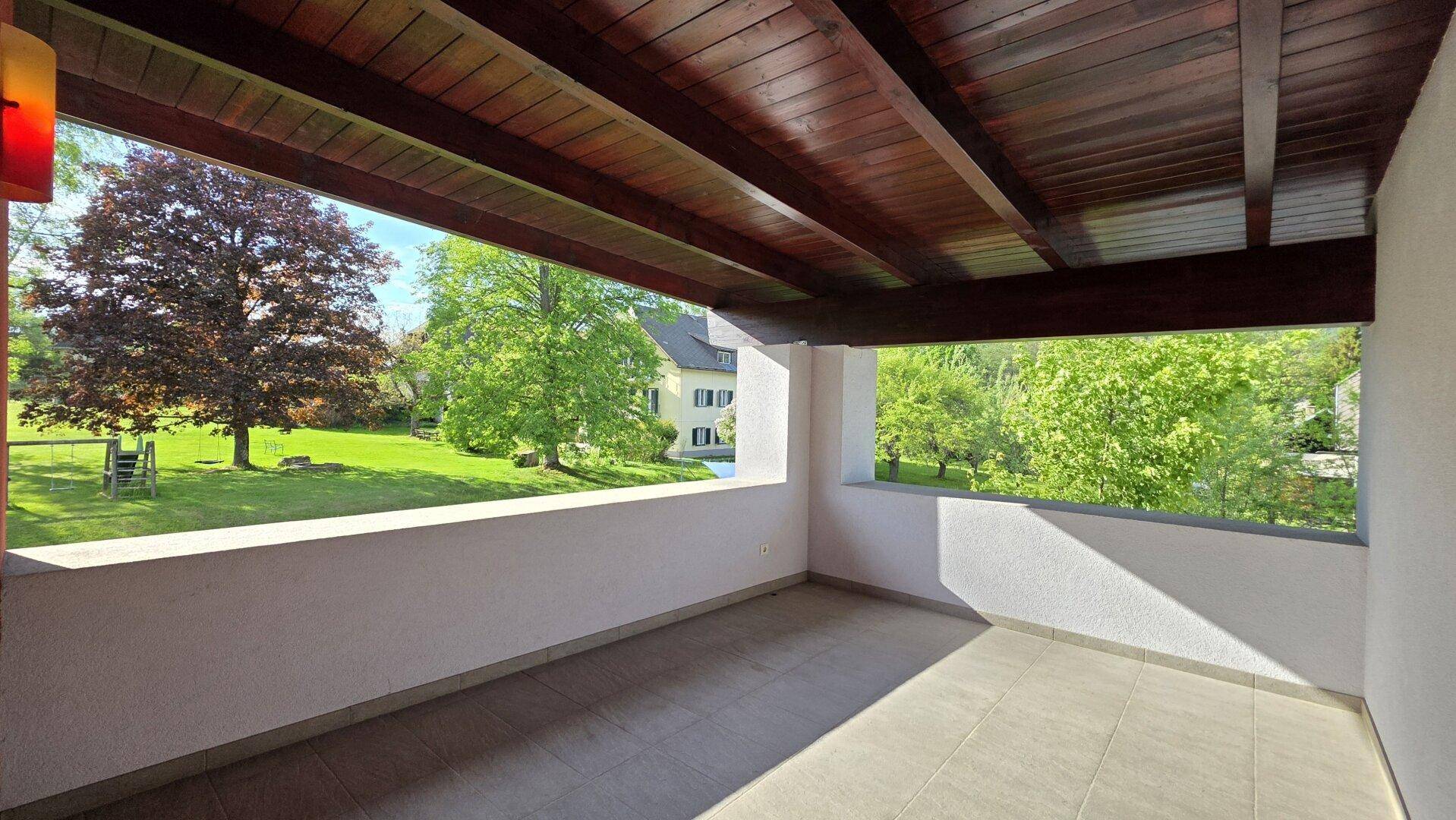 Gemütliche überdachte Loggia mit Holzbalkendecke und Blick auf den weitläufigen Garten.