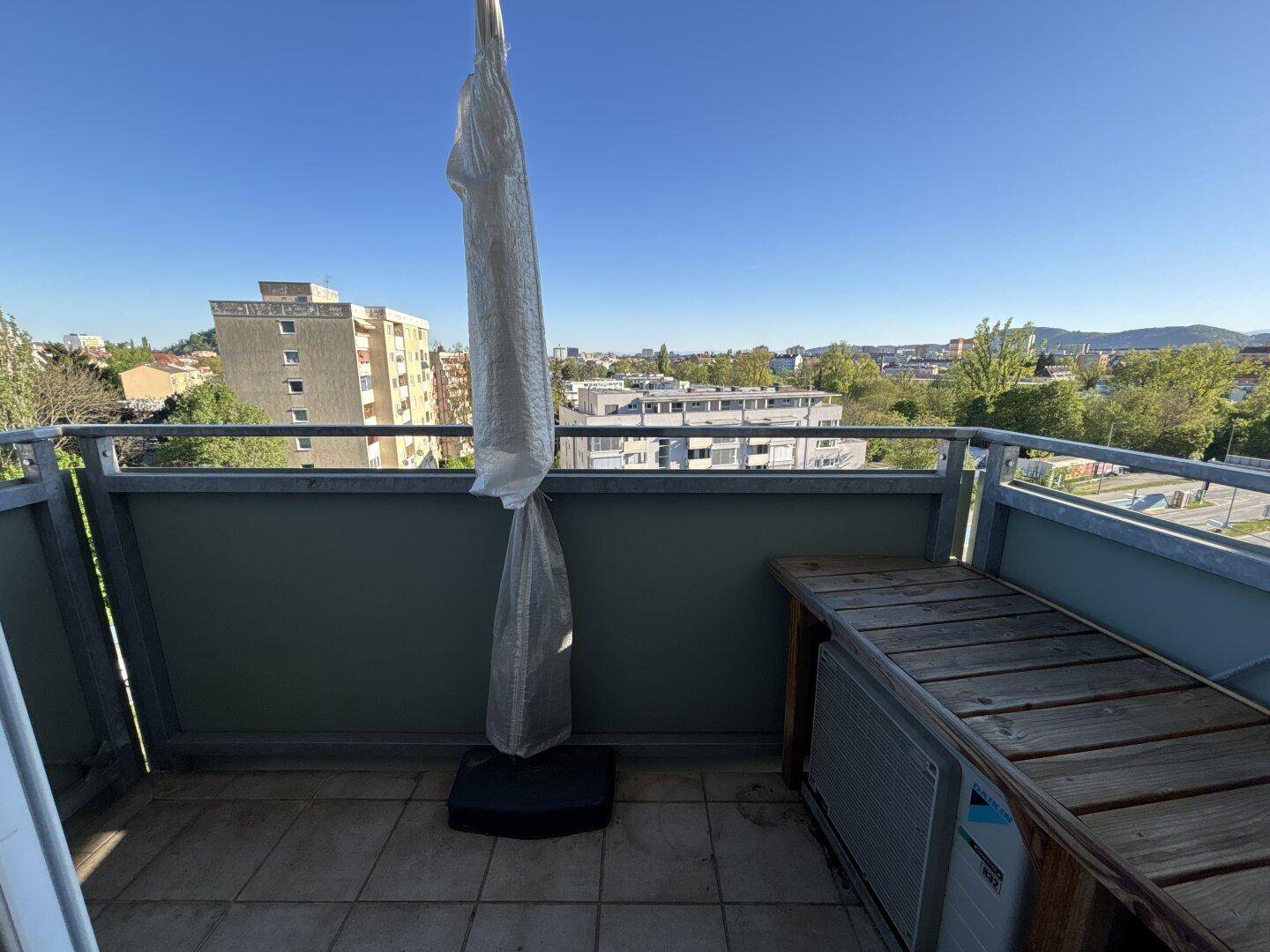 Balkon mit Stadtblick, Fliesenboden und einer Holzbank, ideal zum Entspannen im Freien.