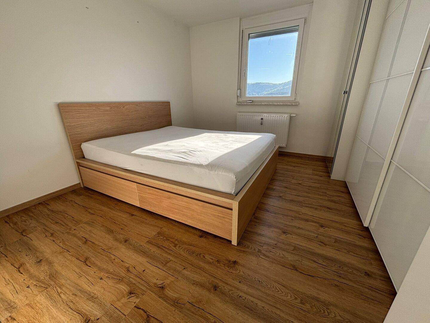 Helles Schlafzimmer mit Holzboden, einem modernen Holzdoppelbett und Fenster mit Ausblick.
