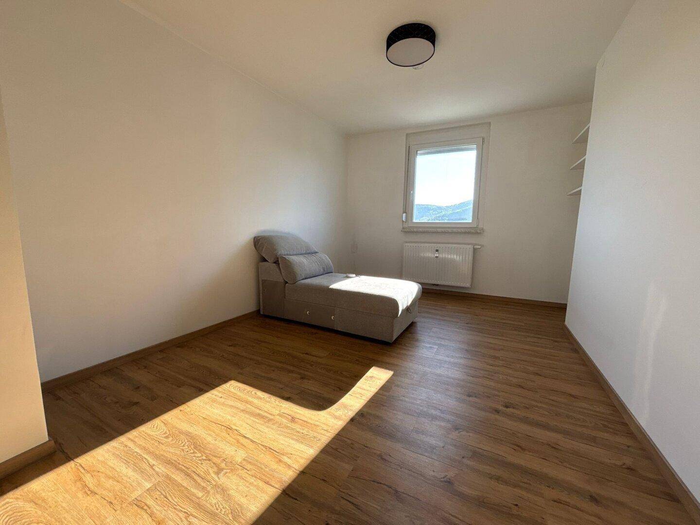 Helles Schlafzimmer mit Holzboden, einem Fenster und einem Liegesofa, ideal zum Entspannen.