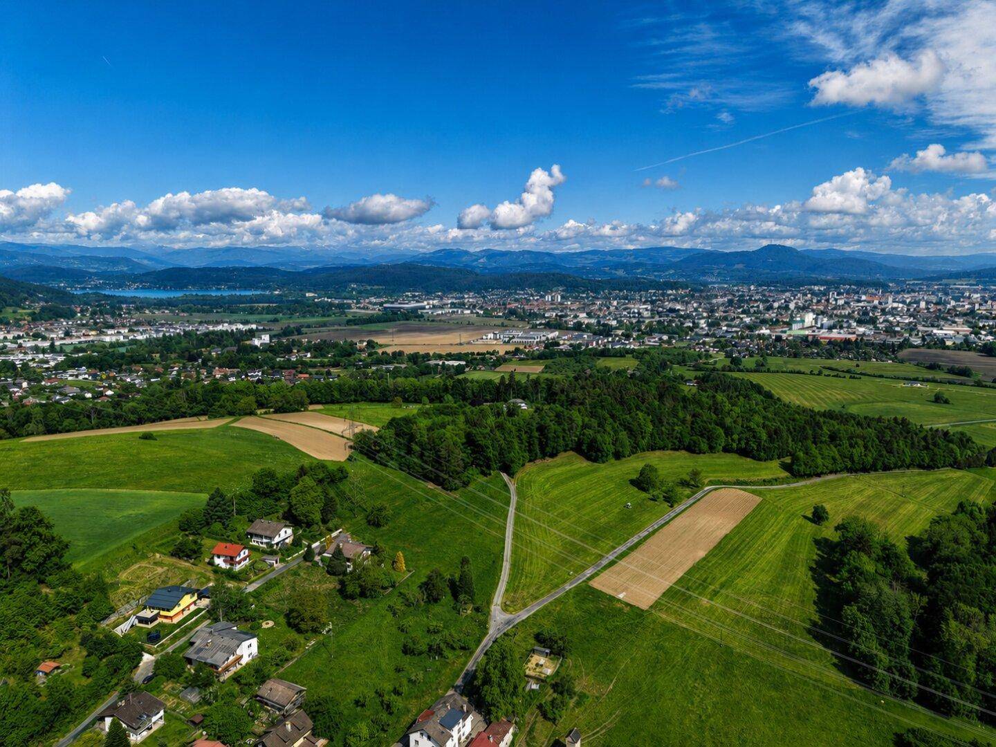 Weitläufige Luftaufnahme der ländlichen Umgebung mit Feldern, Wäldern, einer Stadt und Bergen im Hintergrund.