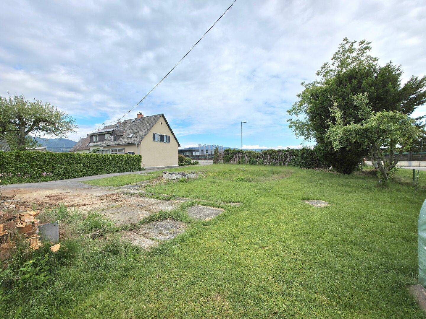 Eine grüne Wiese mit einem Haus und Bergen in der Ferne unter bewölktem Himmel.