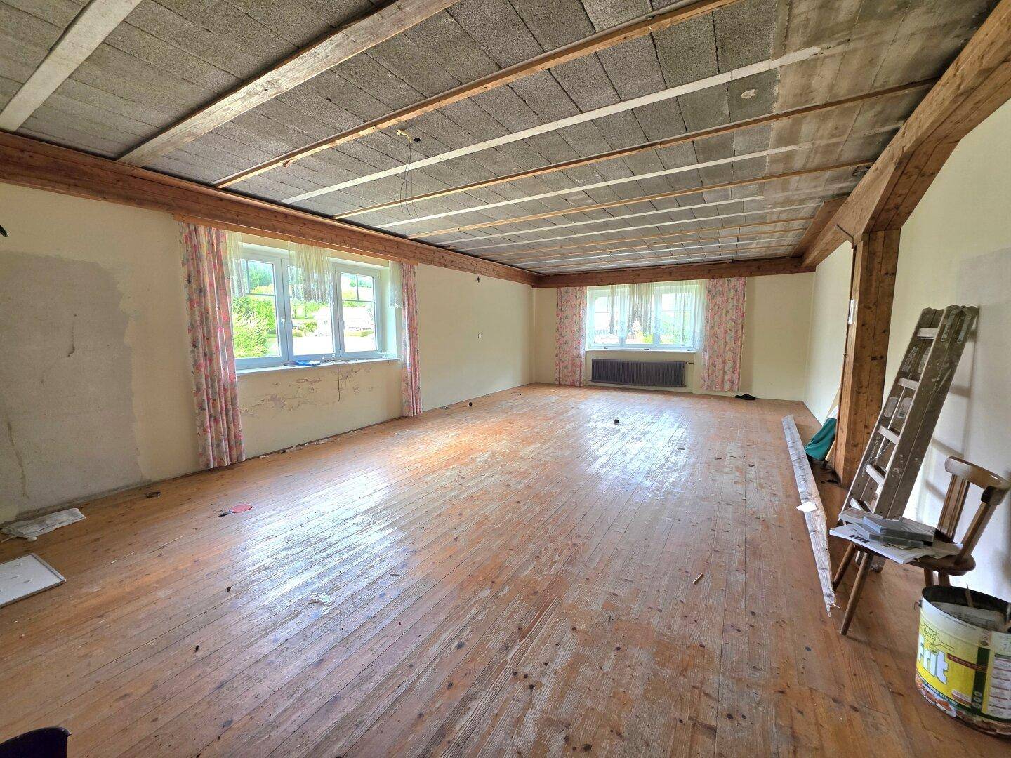 Leerer Raum mit Holzdielenboden, unverputzten Wänden und sichtbaren Deckenbalken, renovierungsbedürftig.
