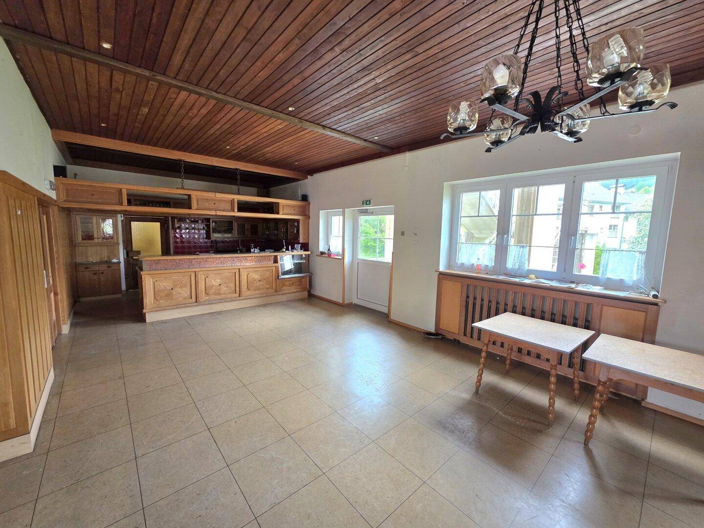Großer Raum mit Holzdecke, Fliesenboden und einer integrierten Holztheke mit Bar.