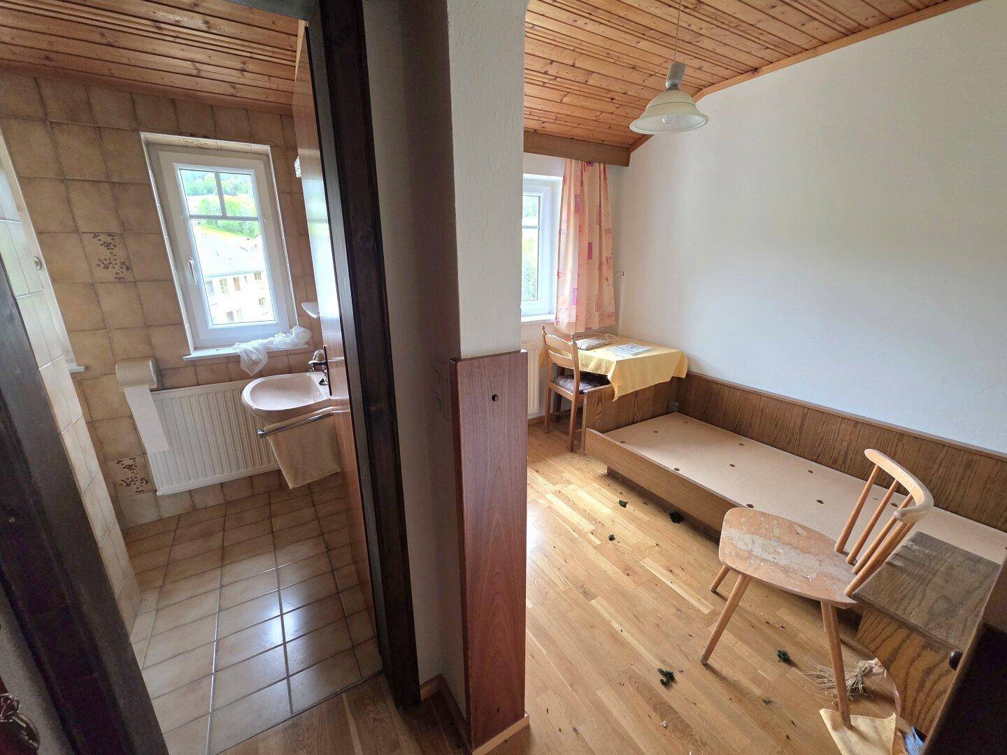 Schlafzimmer mit Holzdielenboden, Holzdecke und angrenzendem Badezimmer.