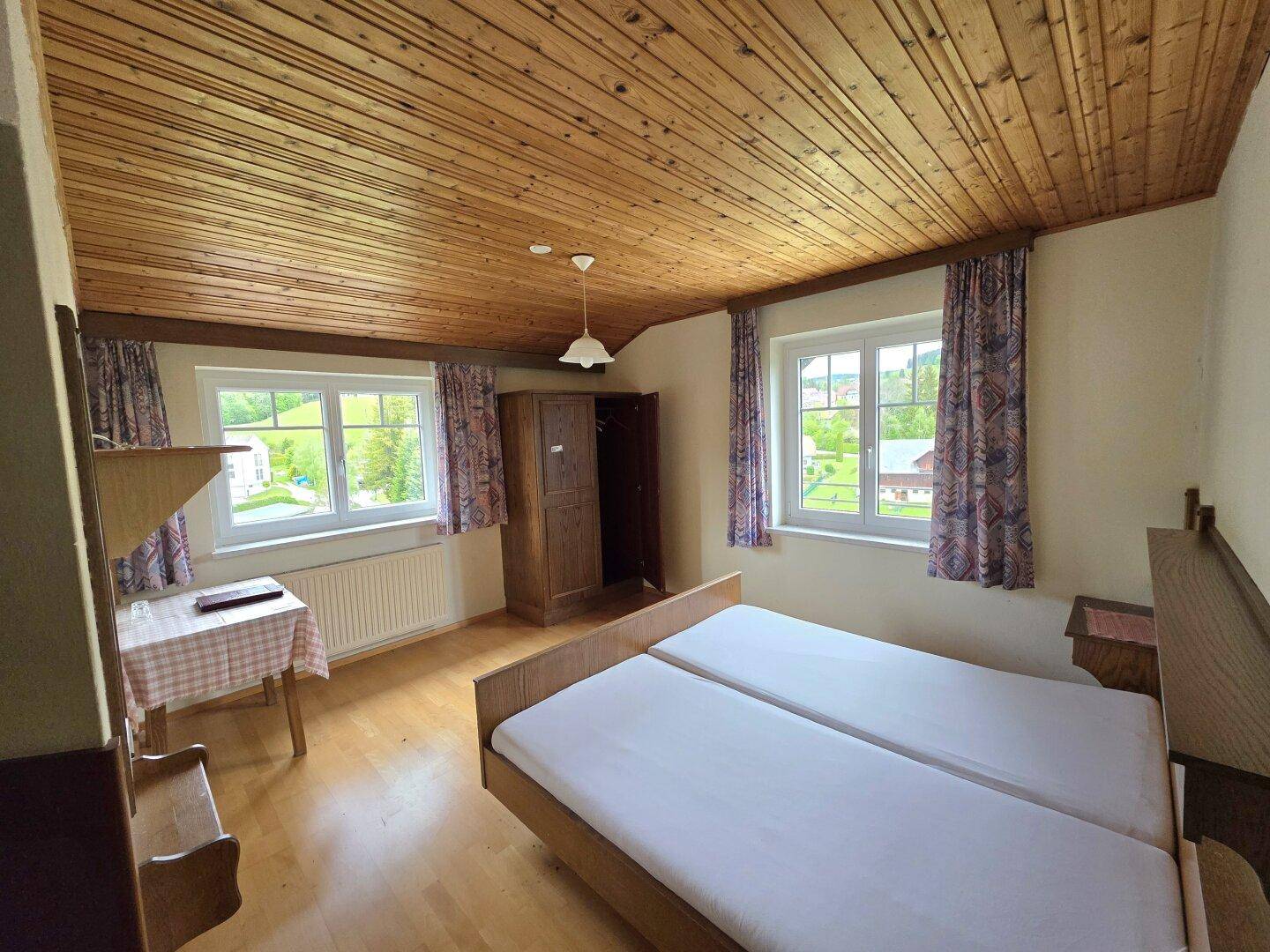 Helles Schlafzimmer mit Holzdielenboden, Holzdecke und zwei Einzelbetten mit Blick ins Grüne.