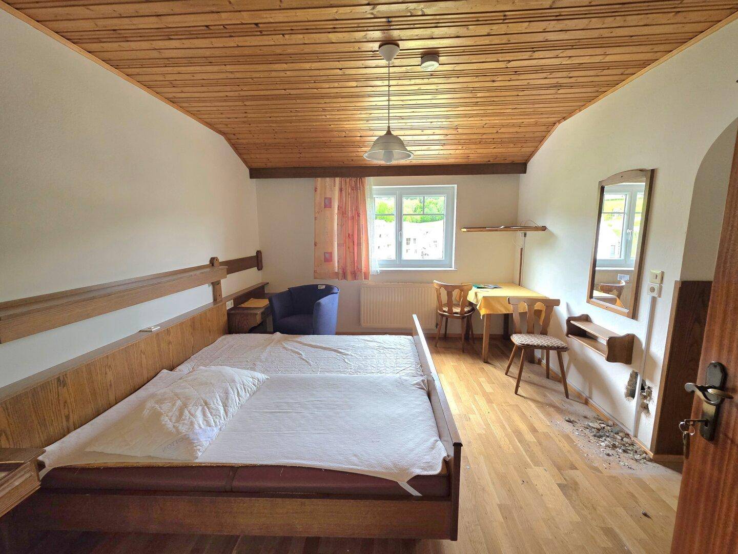 Schlafzimmer mit Holzdielenboden, Holzdecke und zwei Einzelbetten sowie einem kleinen Tisch.