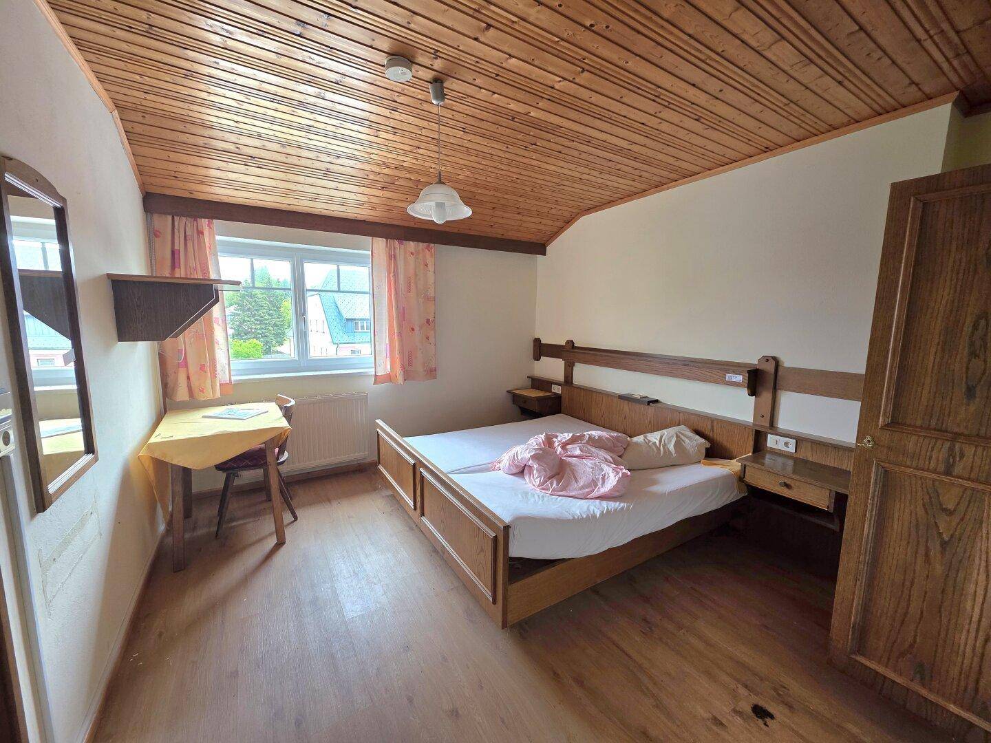 Schlafzimmer mit Holzdielenboden, Holzdecke und einem Doppelbett sowie einem Schreibtisch.