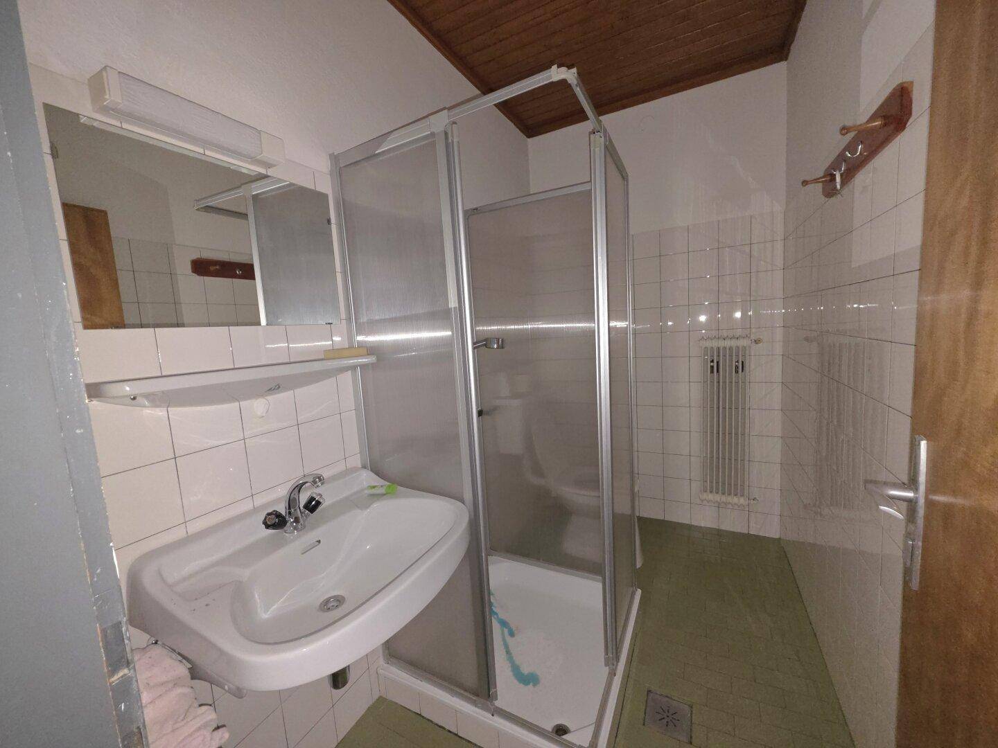Badezimmer mit weißen Fliesen, Duschkabine und Waschbecken, in einfachem Zustand.