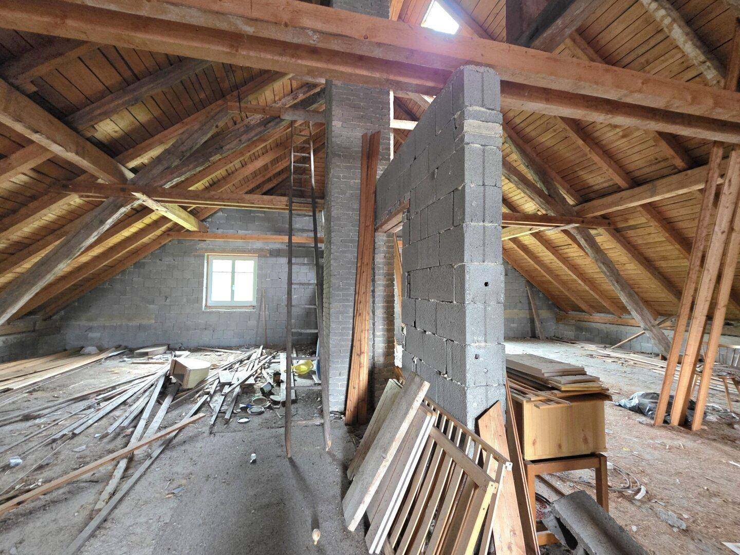 Dachbodenbereich mit freiliegenden Holzbalken und einer Leiter, bereit für die weitere Entwicklung.