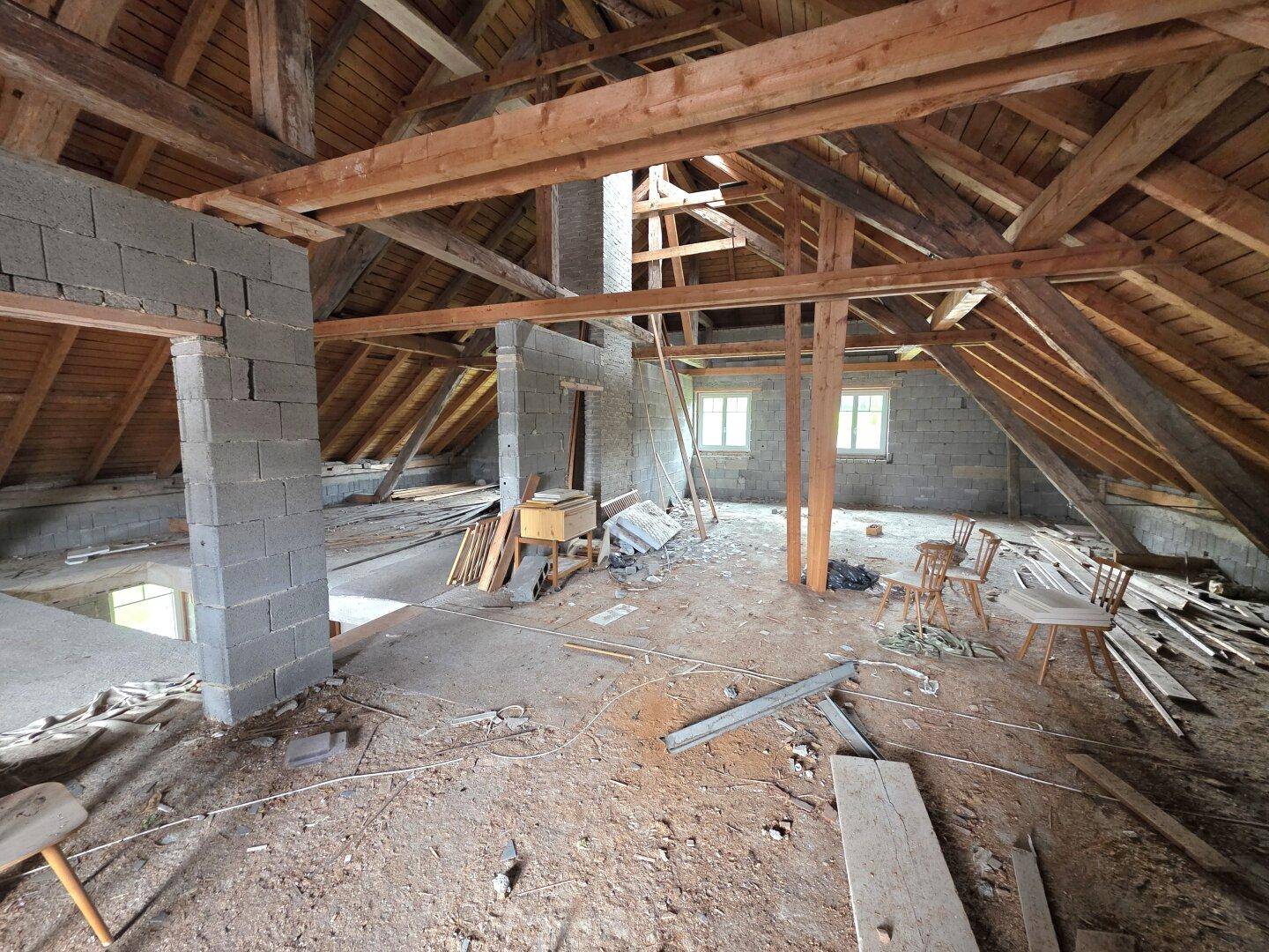 Geräumiger Dachboden mit sichtbaren Holzbalken und Fenstern, ideal für einen zukünftigen Ausbau.