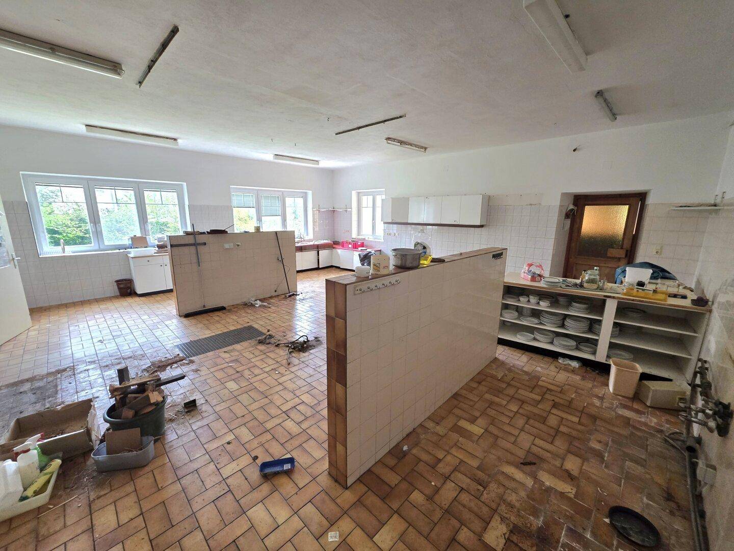 Große, geflieste Küche mit mehreren Arbeitsbereichen und Fenstern, die viel Licht hereinlassen.