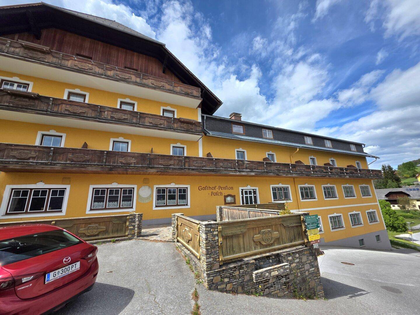 Fassade eines traditionellen Gasthofs mit gelbem Anstrich, Holzbalkonen und Fenstern.