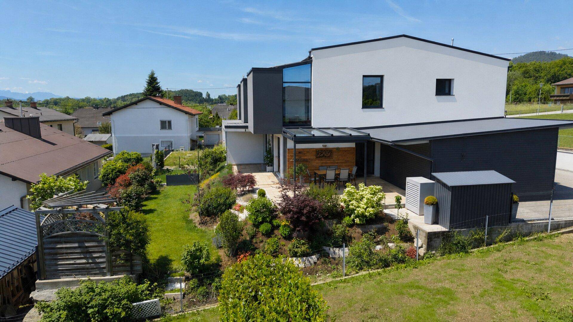 Luftaufnahme des modernen Hauses mit großem, gepflegtem Garten und Carport.