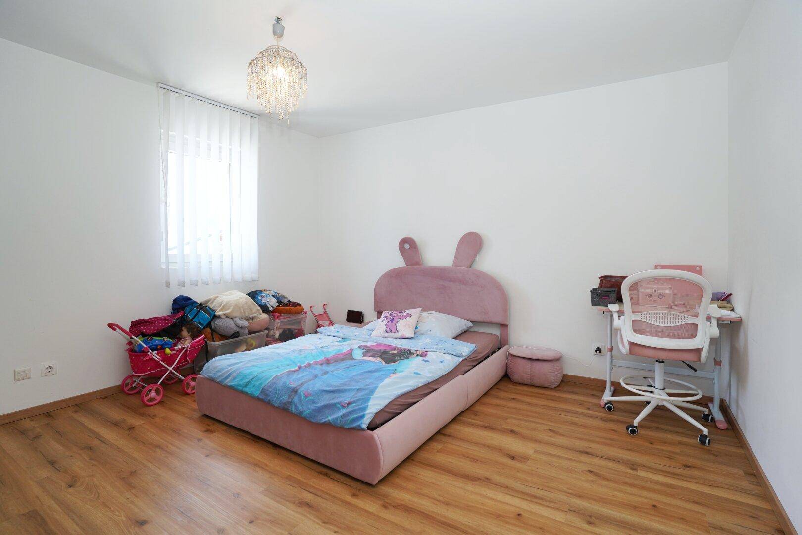 Kinderzimmer mit rosa Hasenbett, Schreibtisch und Holzoptik-Boden.