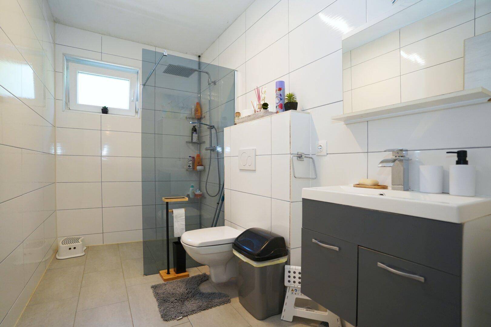 Modernes Badezimmer mit ebenerdiger Dusche, Waschtisch und Fenster.