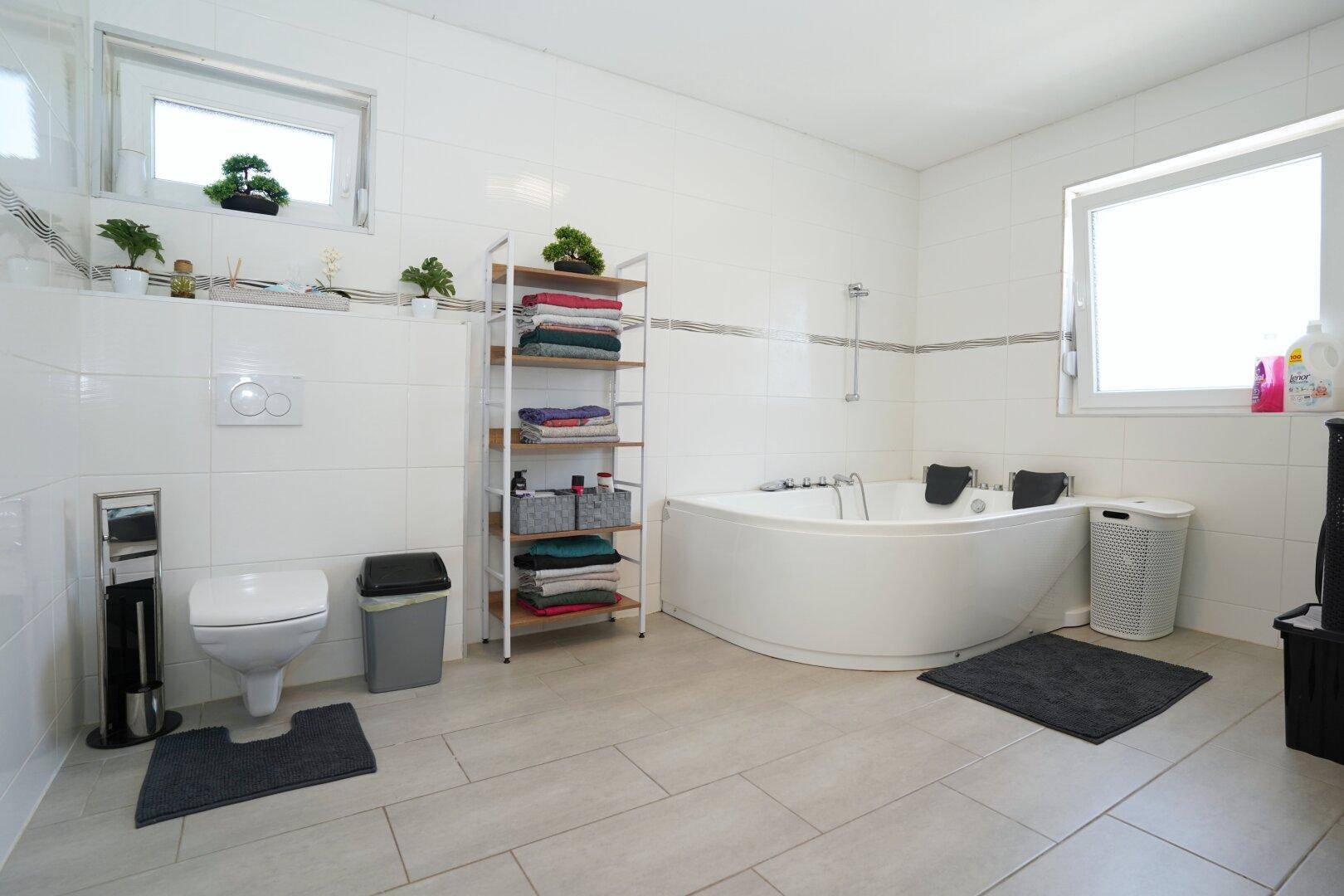 Geräumiges Badezimmer mit Eckbadewanne, wandhängendem WC und zwei Fenstern.