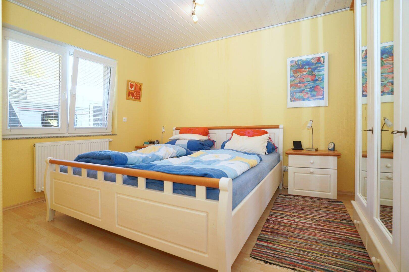 Helles Schlafzimmer mit Doppelbett, gelben Wänden und Laminatboden.