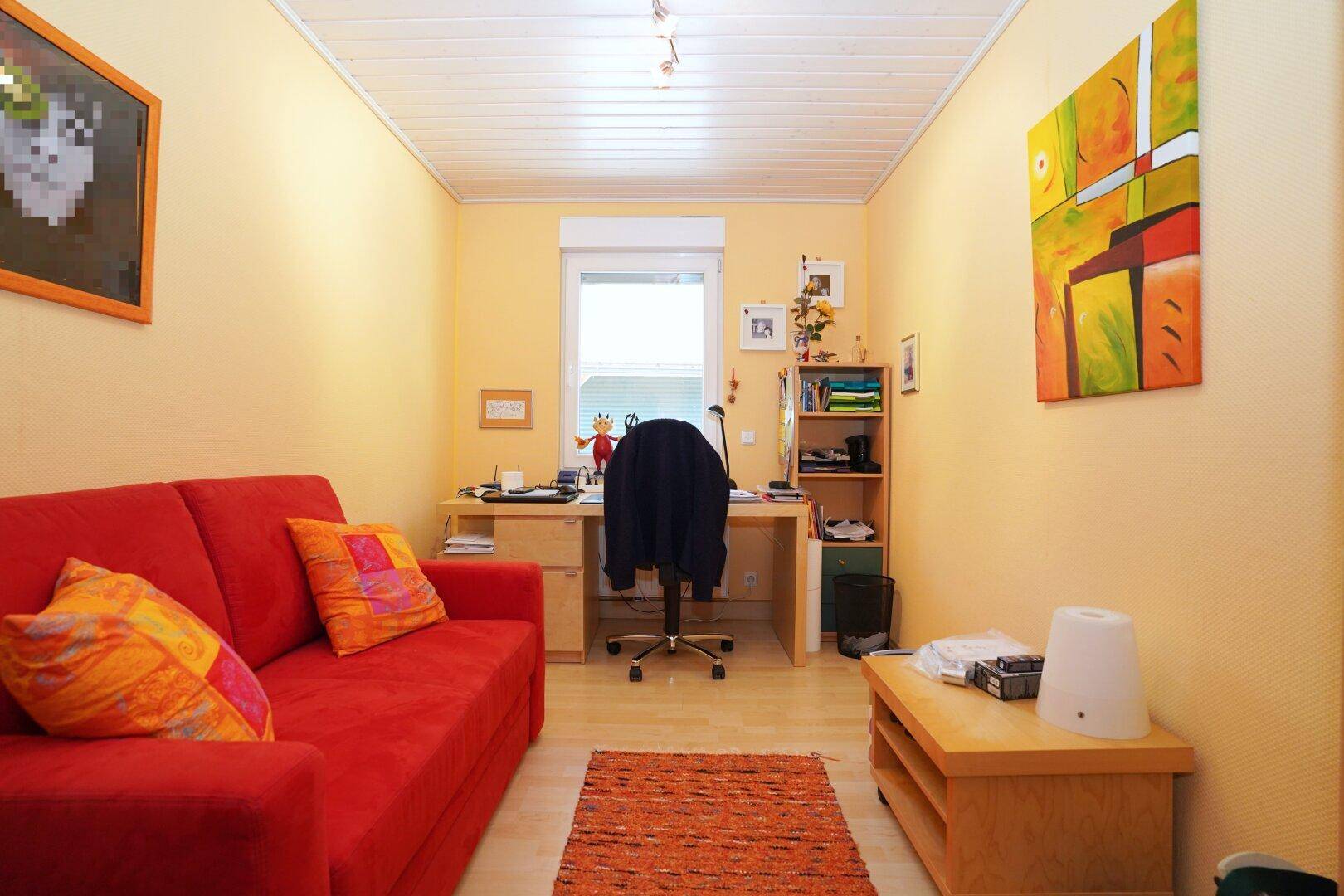 Arbeitszimmer mit Schreibtisch, rotem Sofa und Blick ins Grüne.