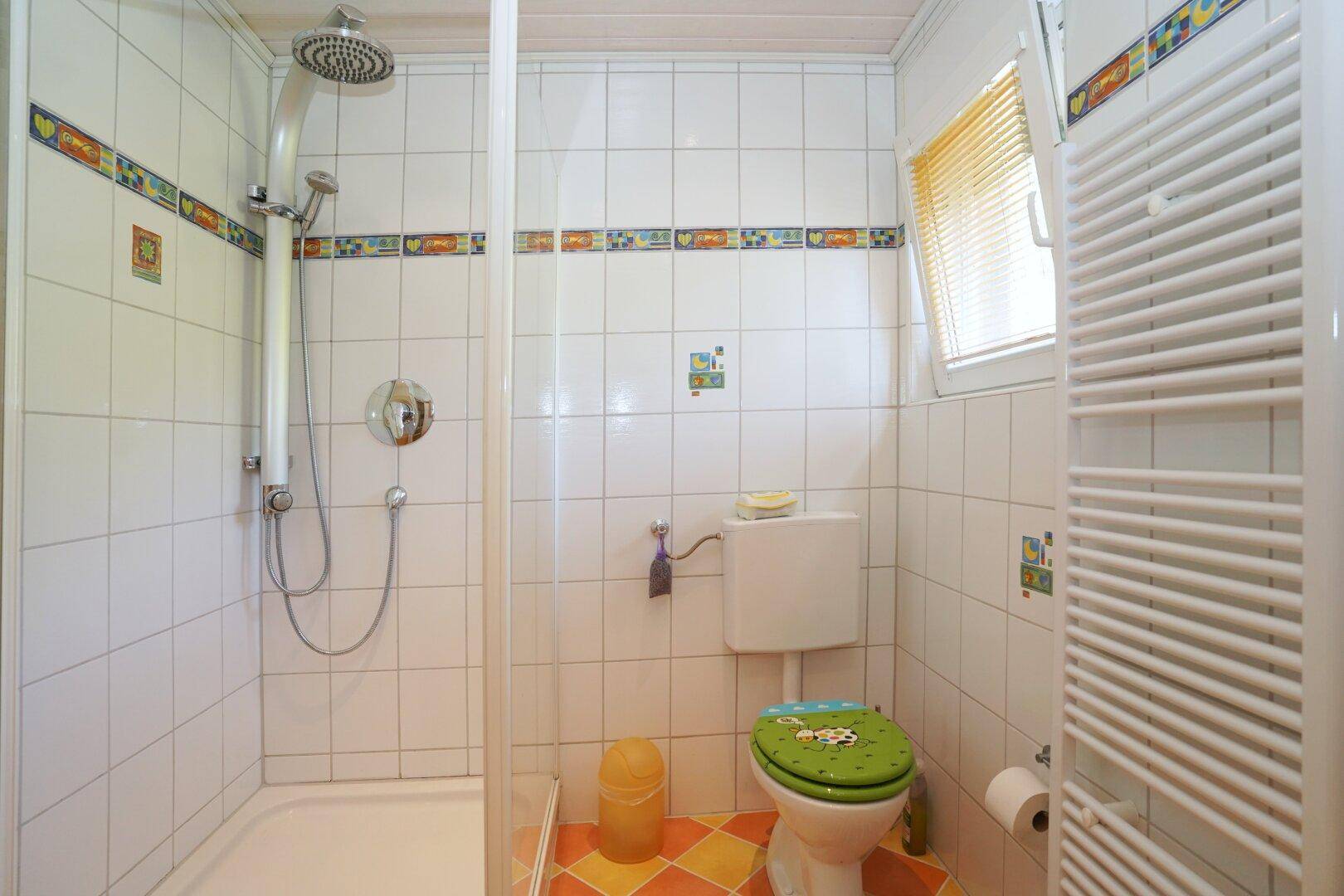 Badezimmer mit Duschkabine, WC und farbenfrohen Fliesen.