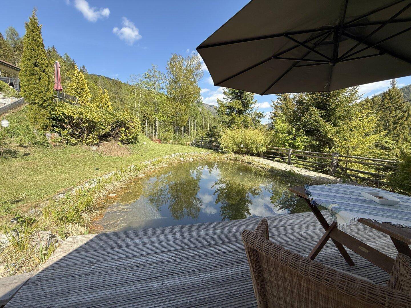 Holzterrasse am Teich mit Gartenmöbeln und Blick auf die umliegende Natur.