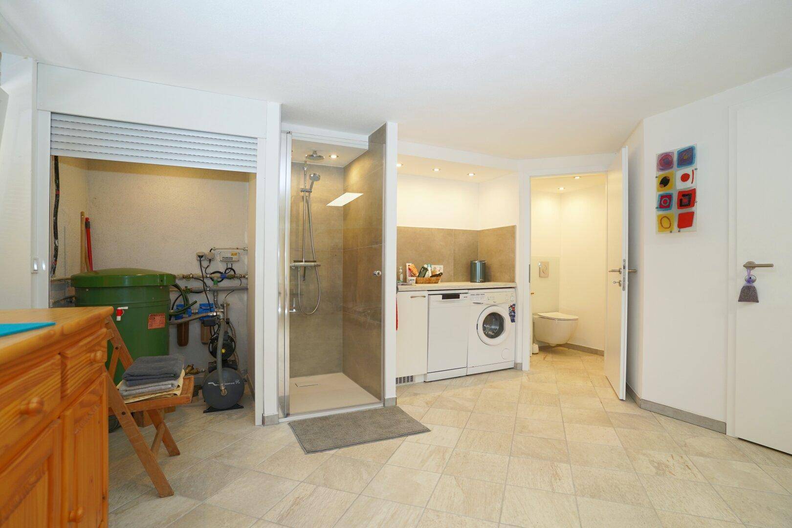Hauswirtschaftsraum im Untergeschoss mit Waschmaschine, Trockner und Duschbereich.