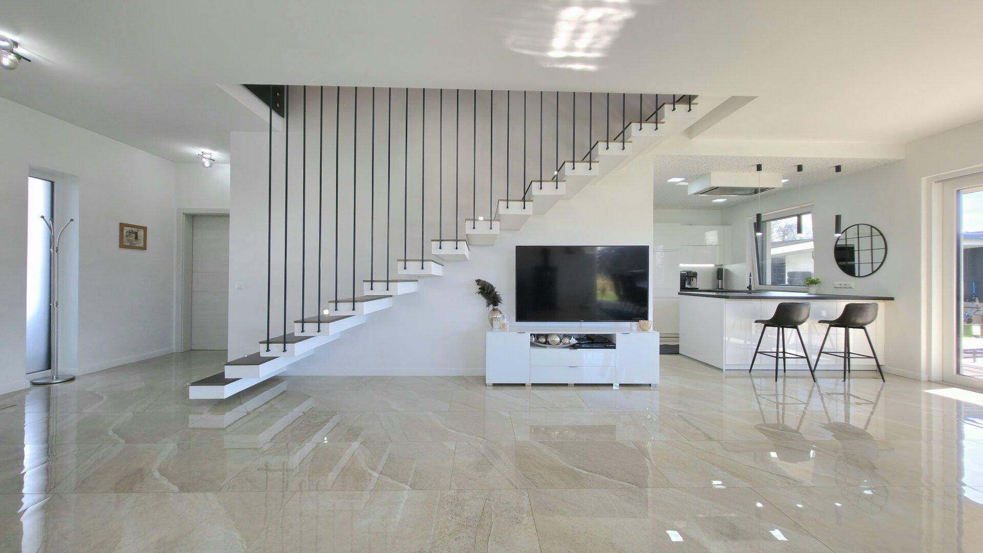 Geräumiger Wohnbereich mit offener Küche, moderner Treppe und glänzendem Fliesenboden.