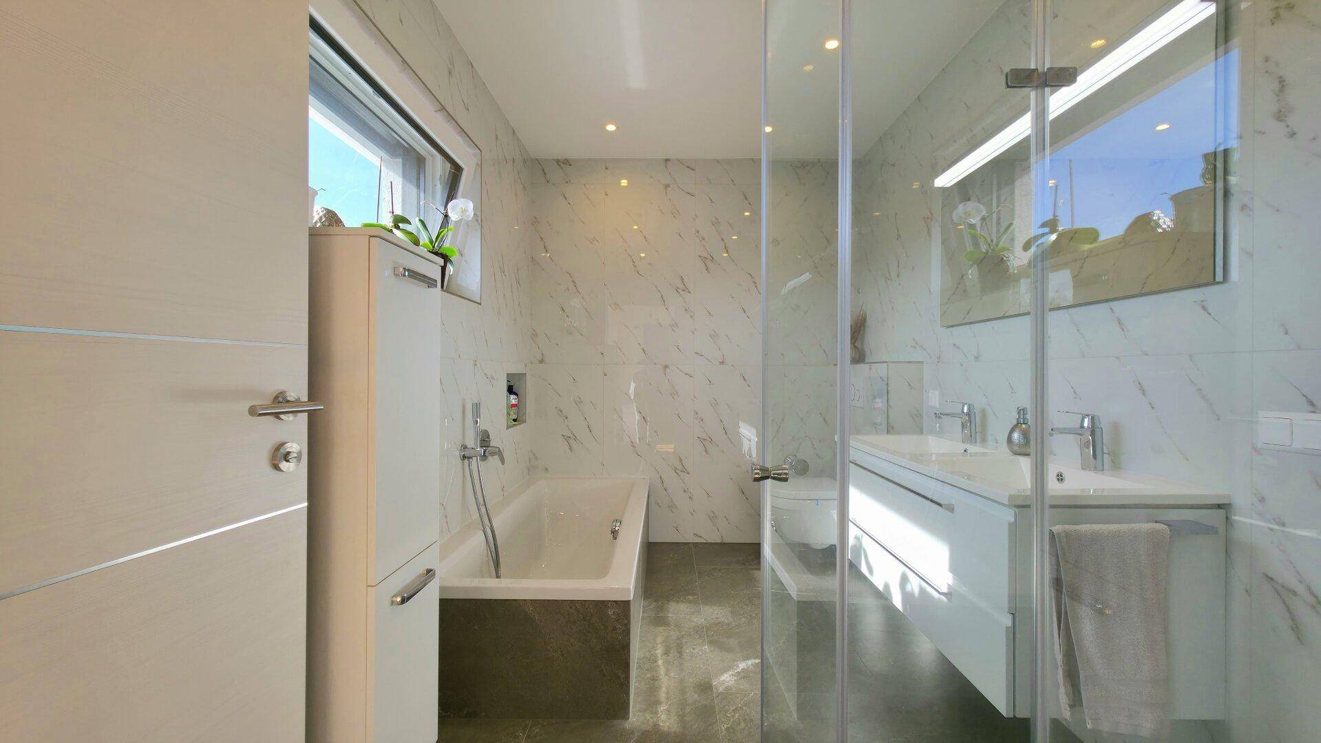 Modernes Badezimmer mit Marmorfliesen, Badewanne, Doppelwaschbecken und großer Dusche.