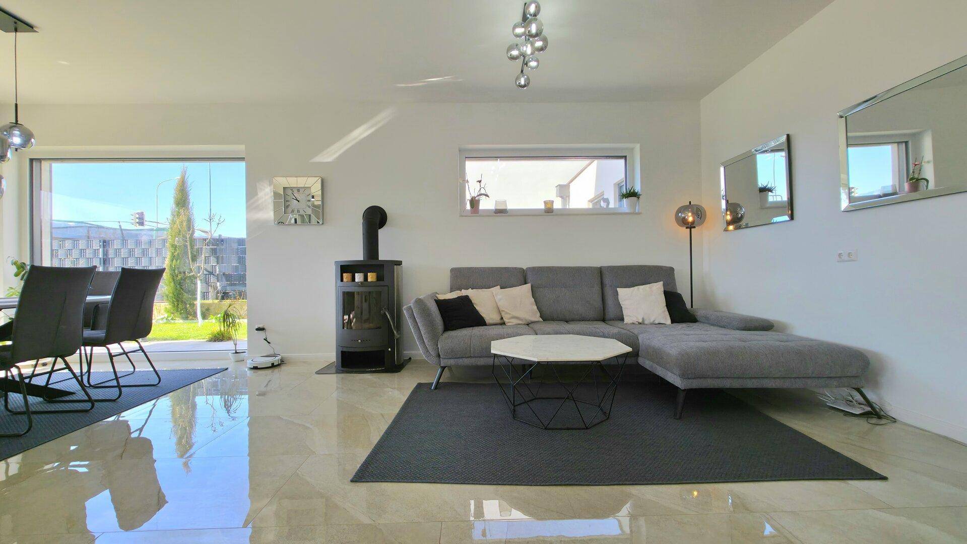 Gemütliches Wohnzimmer mit modernem Sofa, Kaminofen und großen Fenstern zum Garten.