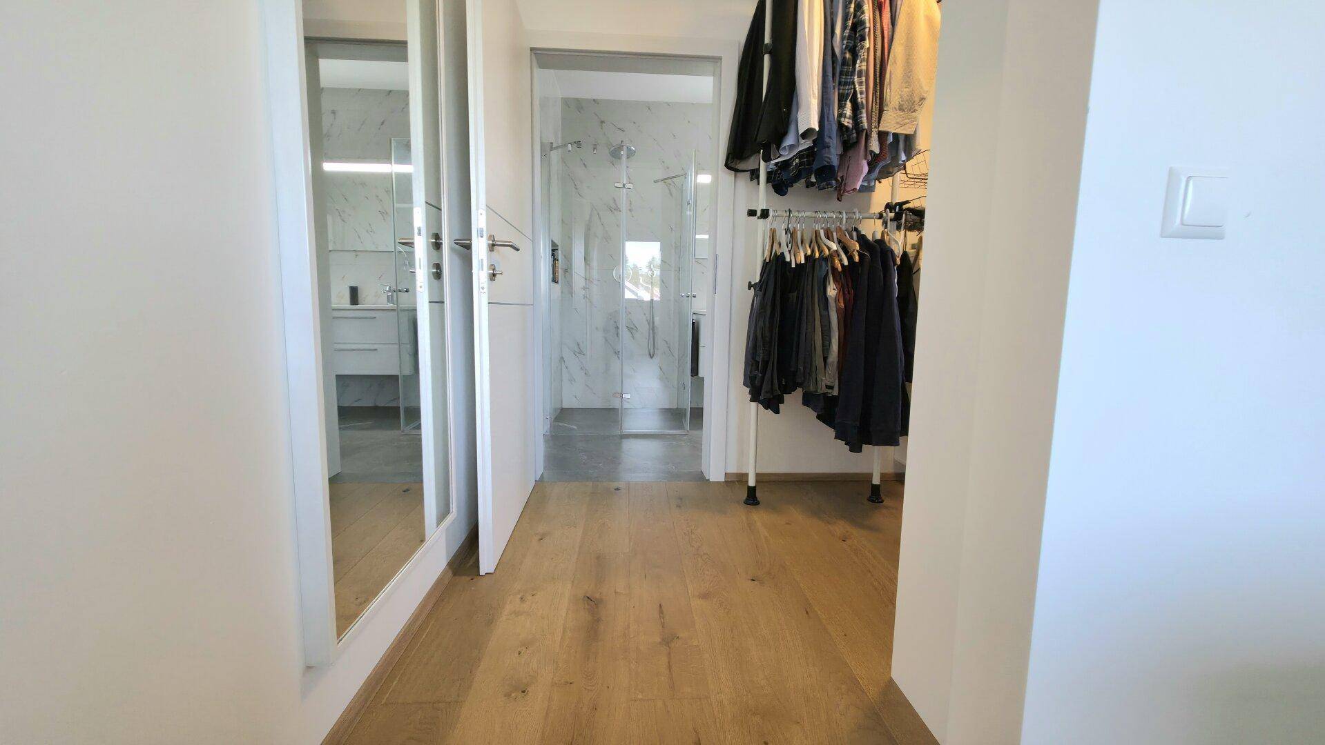 Heller Flur mit Holzboden, offenem Kleiderständer und Zugang zum modernen Badezimmer.