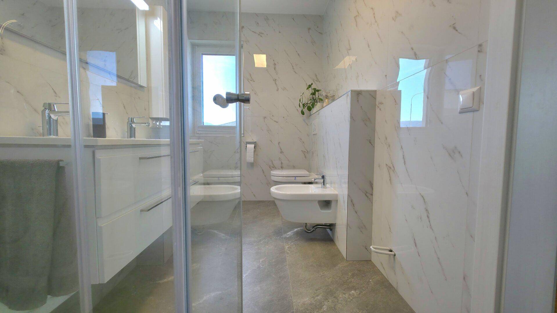 Modernes Badezimmer mit Marmorfliesen, bodengleicher Dusche, Toilette und Bidet.