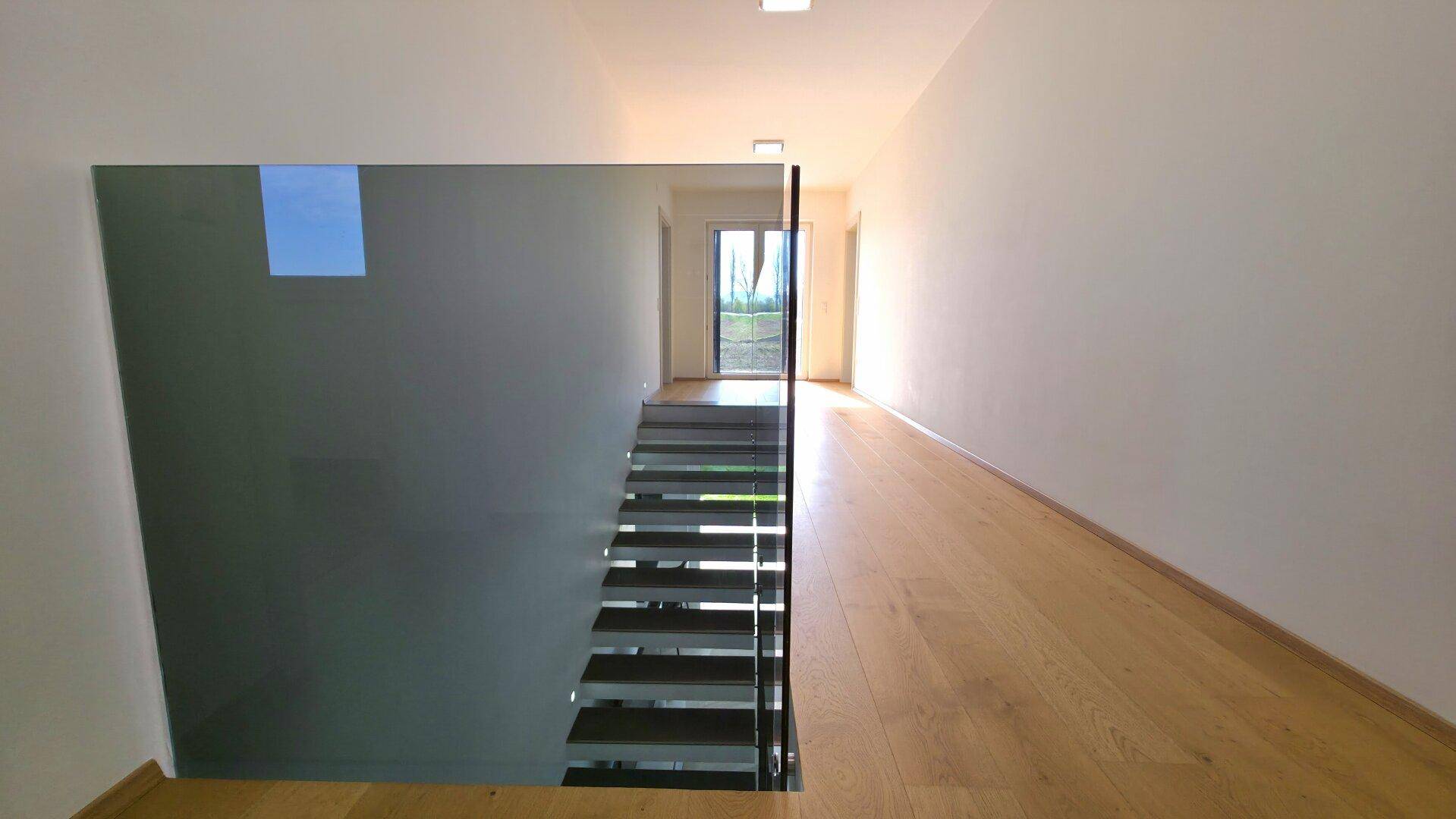 Heller Flur im Obergeschoss mit Holzboden und Blick auf die moderne Treppe.