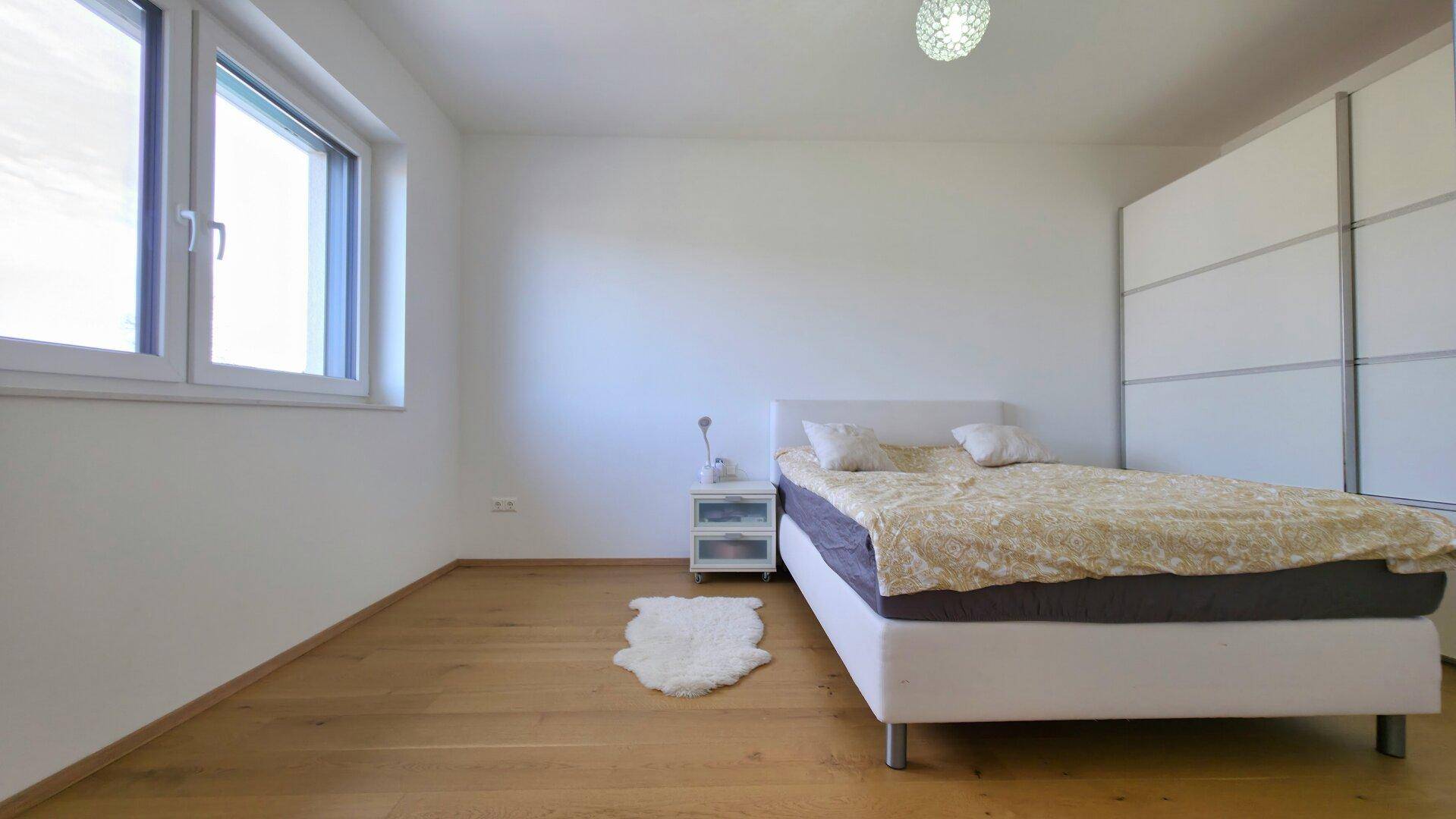 Helles Schlafzimmer mit Holzboden, großem Fenster und weißem Kleiderschrank.