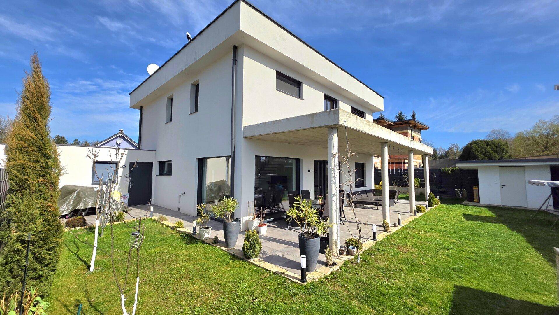 Modernes Haus mit großer überdachter Terrasse und sonnigem, gepflegtem Garten.