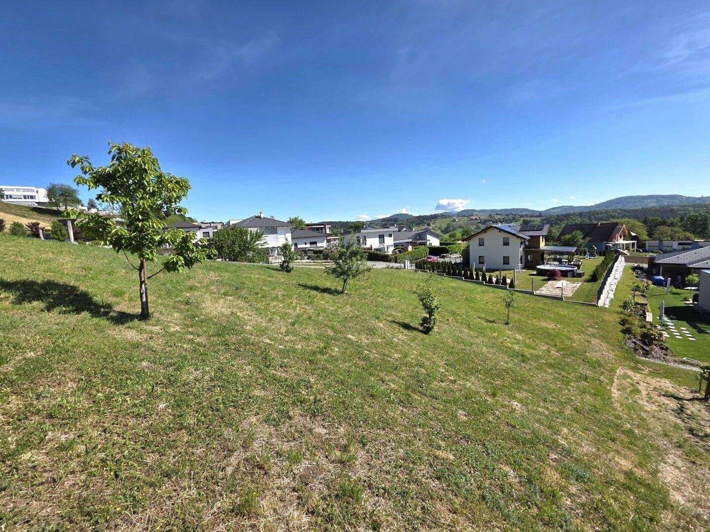 Panoramablick über eine grüne Hügellandschaft mit verstreuten Wohnhäusern und weitem Horizont.