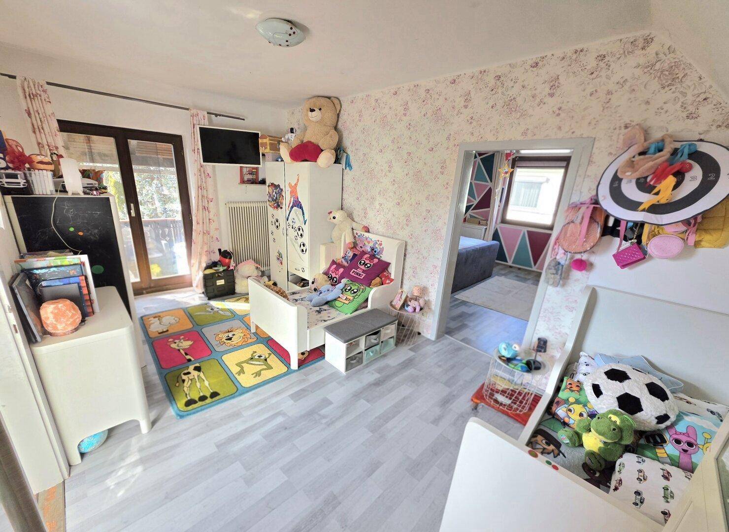 Kinderzimmer mit zwei Betten, Spielzeug und Zugang zu einem Balkon.